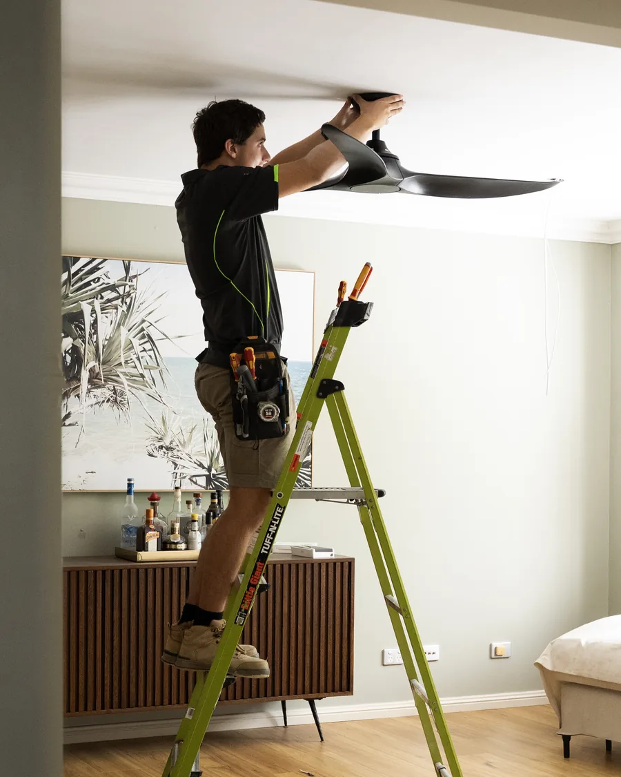 Fix Electrical electrician on a ladder installing a ceiling fan in a living room